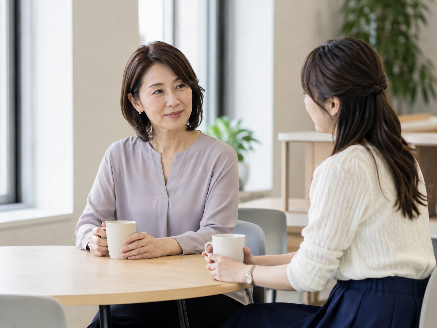 休憩スペースで同僚と落ち着いて話しながら仕事の頼み方を考える場面